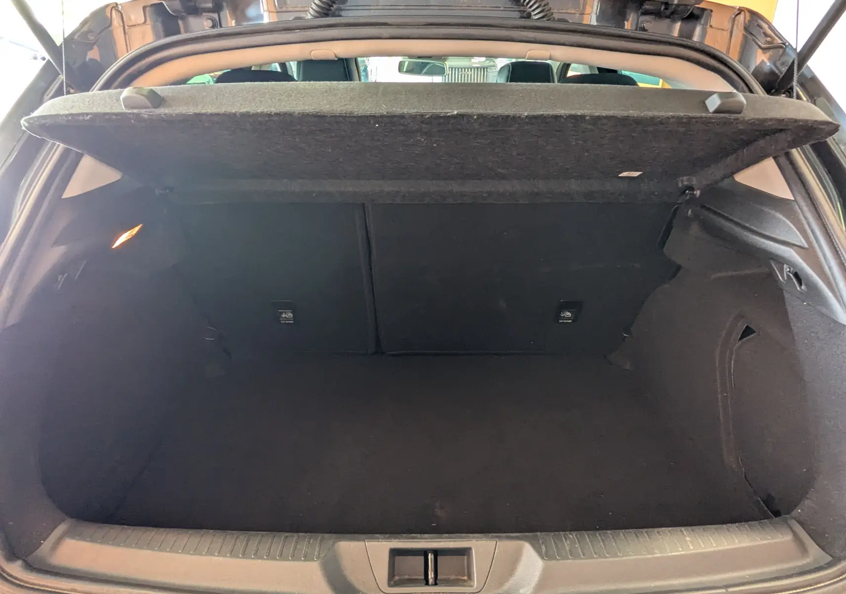 Coffre ouvert vu de l'arrière d'une Renault Mégane IV gris, montrant l'espace de chargement vide et la tablette cache-bagages relevée.