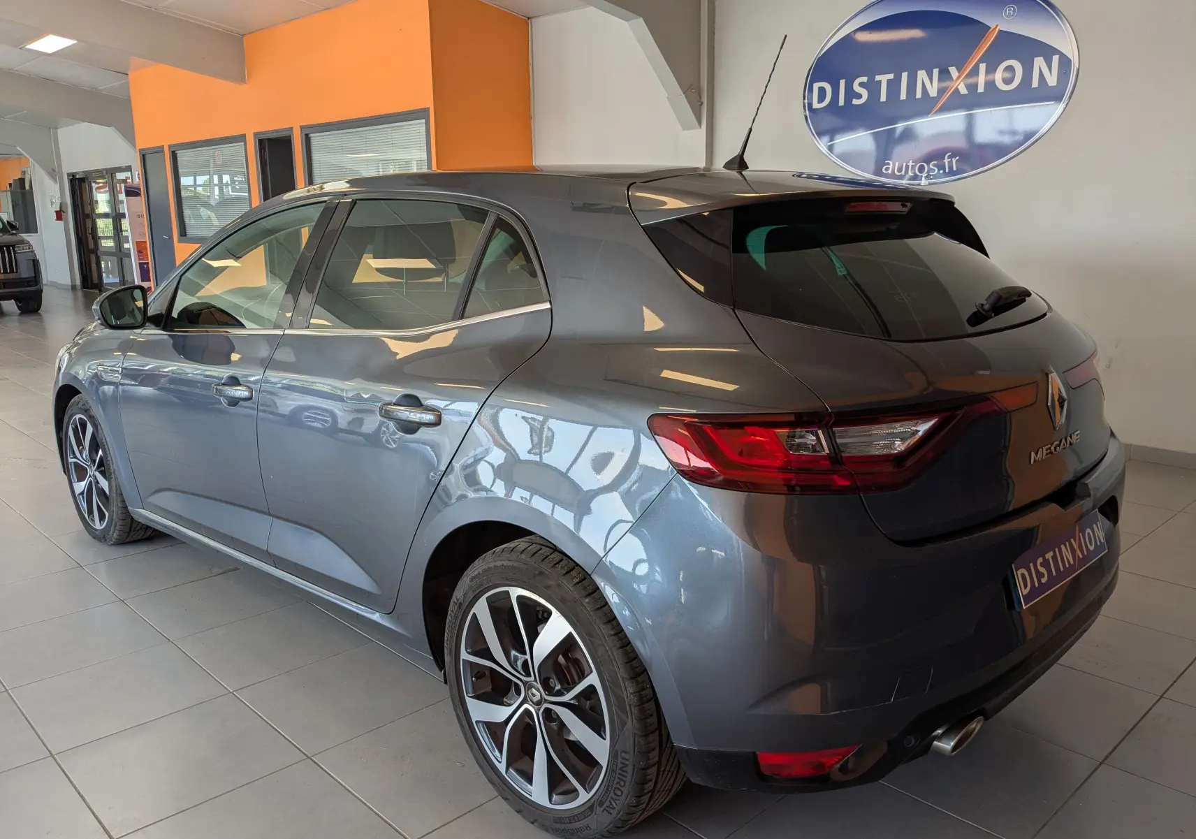 Vue 3/4 arrière droite d'une Renault Mégane IV grise métallisée en intérieur, avec jantes alliage bicolores et feux LED arrière.