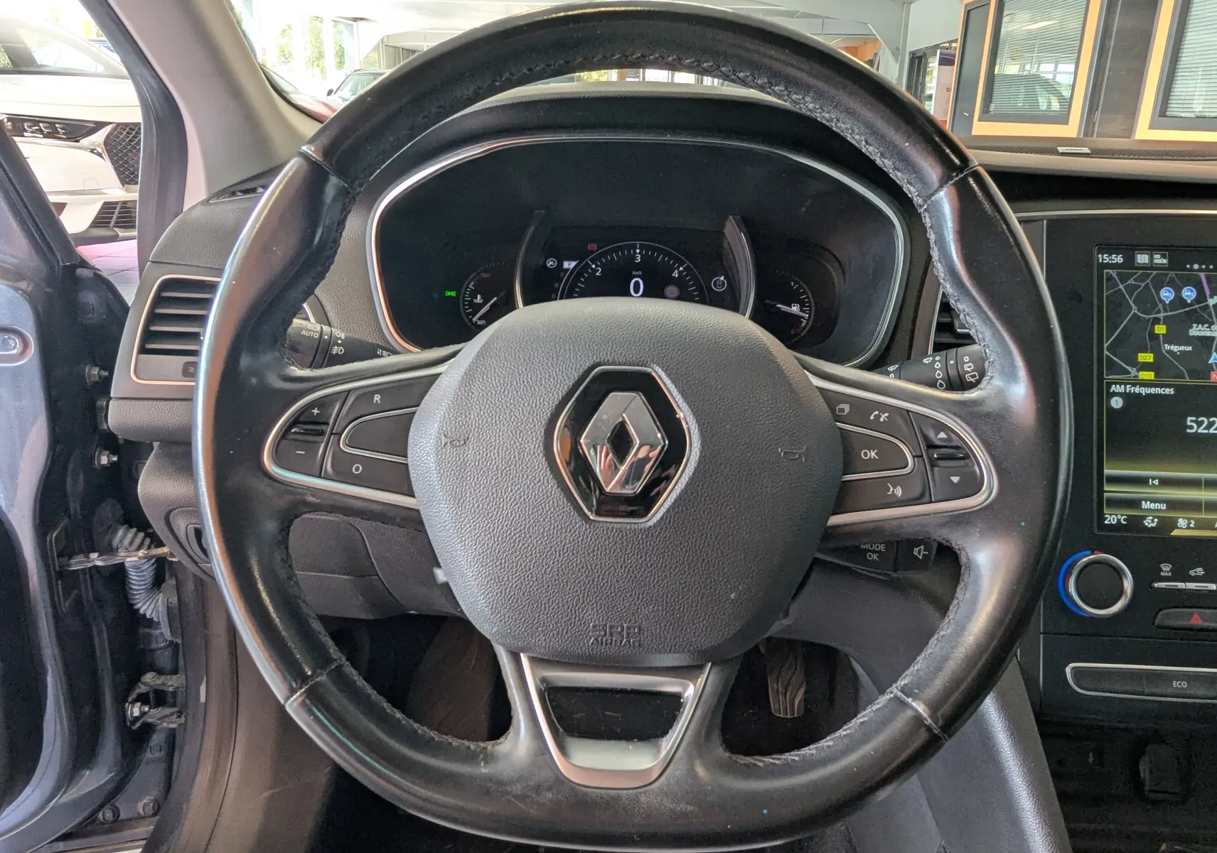 Vue centrée sur le volant en cuir noir de la Renault Mégane IV gris, avec tableau de bord et écran tactile visibles.