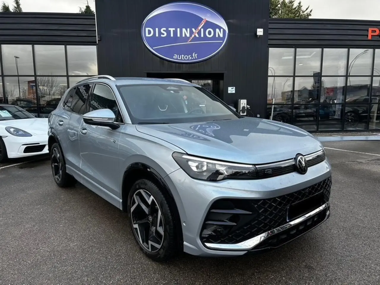 Volkswagen Tiguan III R-Line gris clair en 3/4 avant droit avec jantes alliage noires et calandre noire distinctive.