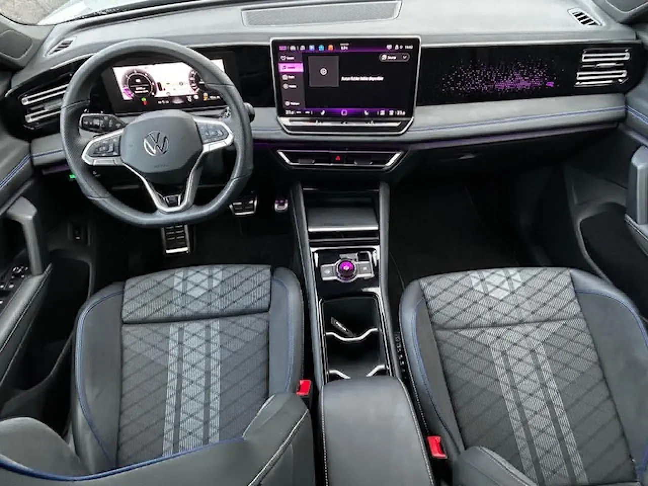 Vue intérieure avant du Volkswagen Tiguan R-Line 2024 avec tableau de bord numérique et sellerie tissu ArtVelours gris à motifs géométriques.
