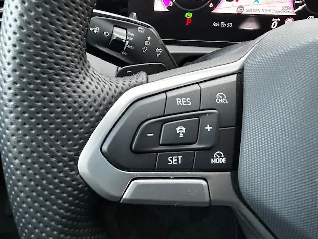 Gros plan sur les commandes de régulateur de vitesse au volant perforé du Volkswagen Tiguan gris clair 2024.