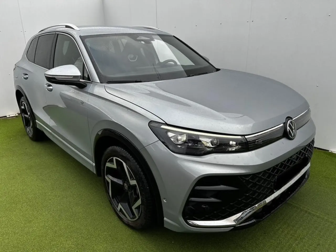 Volkswagen Tiguan III gris clair en 3/4 avant droit avec jantes noires et détails chromés sur calandre et pare-chocs.