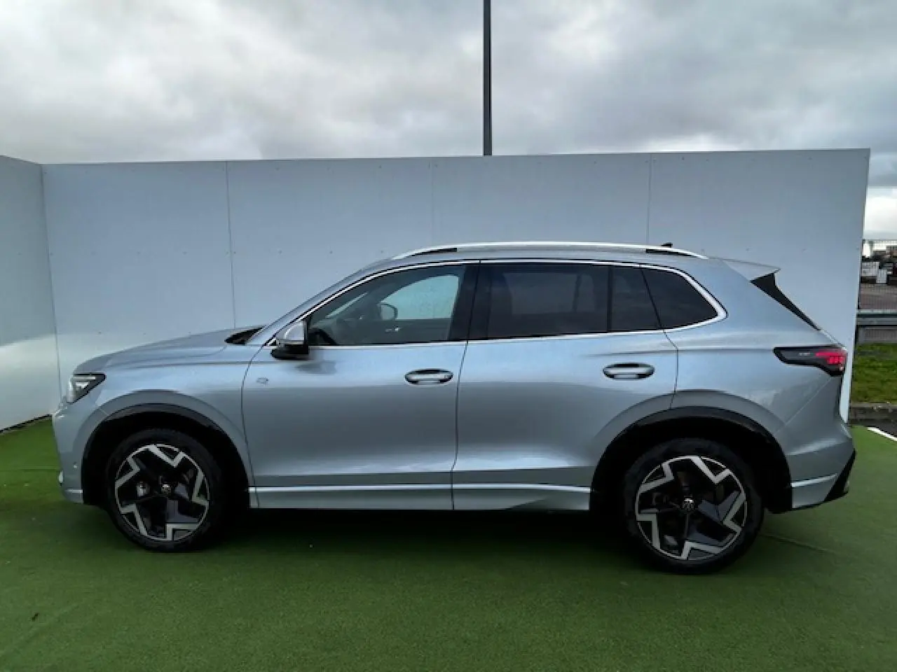 Profil côté gauche du Volkswagen Tiguan III gris clair 2024 avec jantes alliage noires et détails R-Line visibles