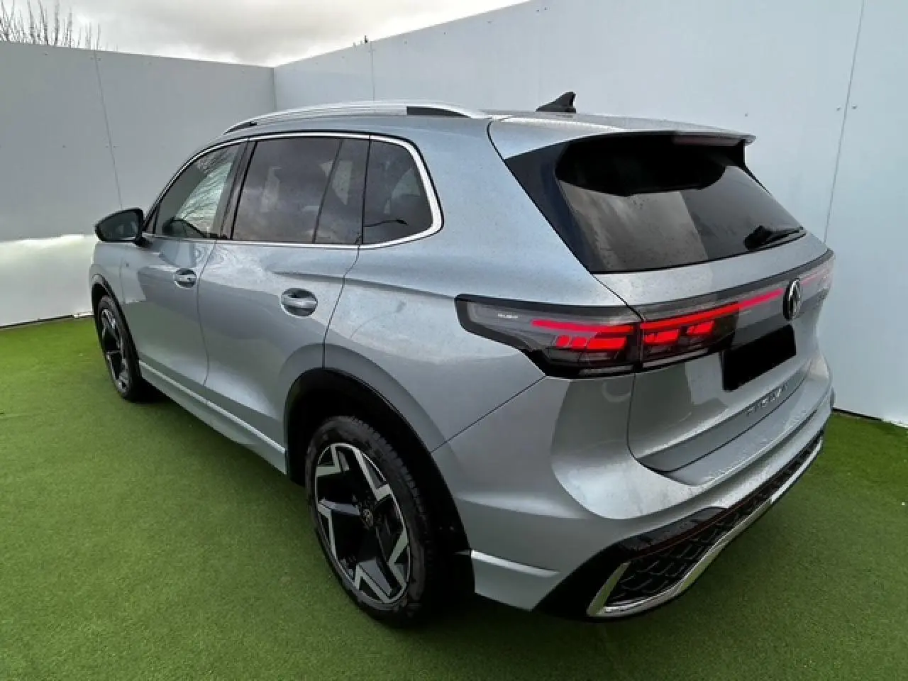 Vue 3/4 arrière droite d'un Volkswagen Tiguan gris clair avec feux arrière LED et jantes noires distinctives.