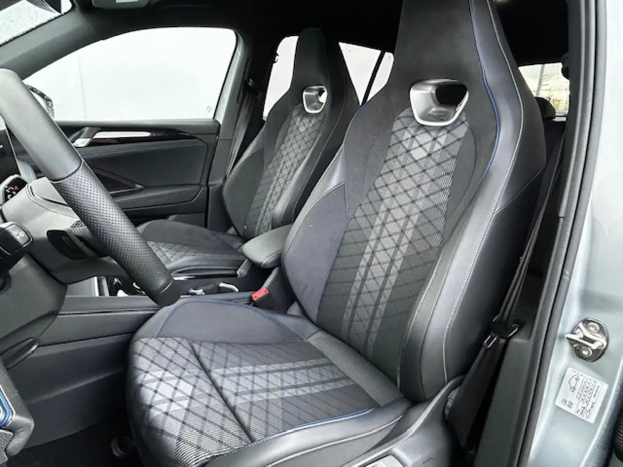Vue intérieure côté conducteur du Volkswagen Tiguan gris clair 2024 avec sièges sport en tissu ArtVelours à surpiqûres bleues.
