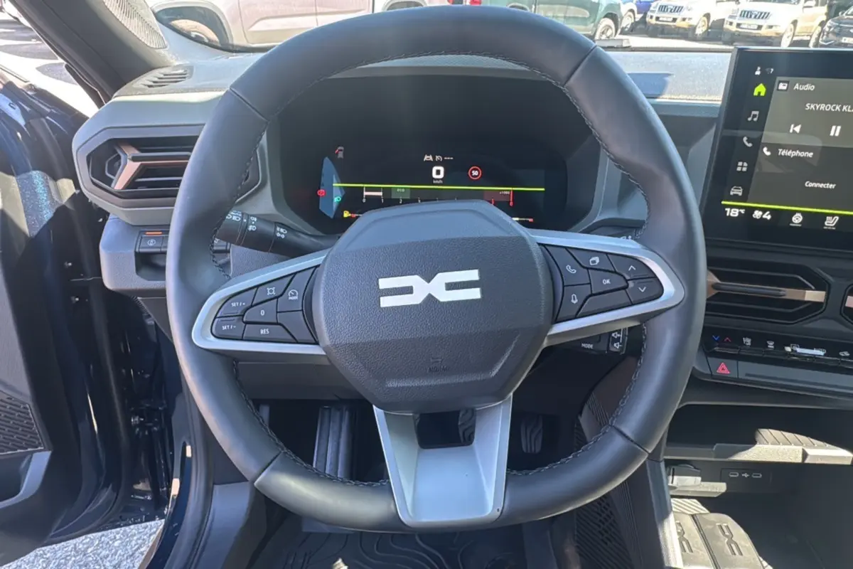 Vue intérieure centrée sur le volant multifonction du Dacia Bigster bleu indigo avec tableau de bord numérique et écran tactile.