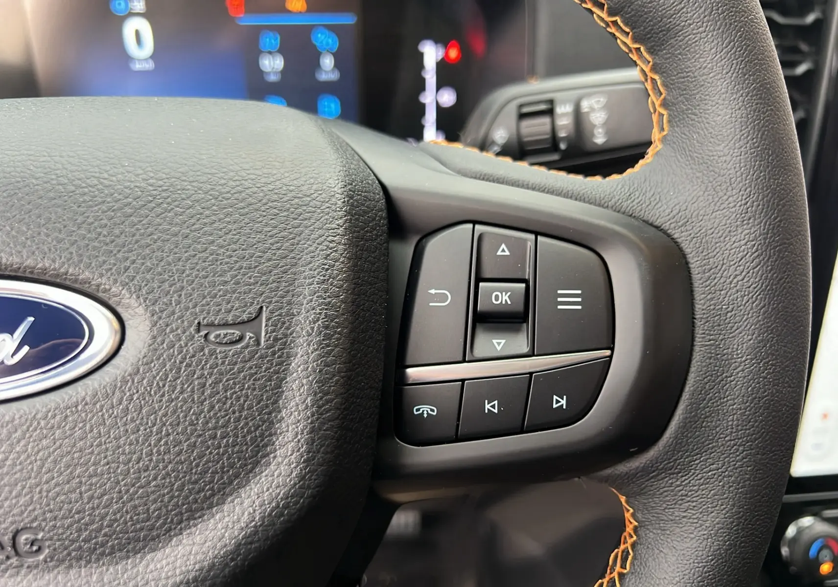Gros plan sur le volant cuir noir avec surpiqûres orange du Ford Ranger 2025, boutons multifonctions visibles à droite.