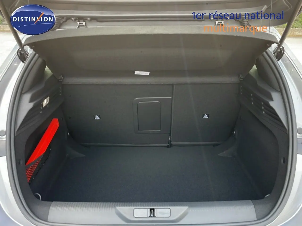 Coffre ouvert vu de l'arrière d'une Peugeot 308 gris Artense métal, avec un triangle de signalisation rouge sur le côté gauche.