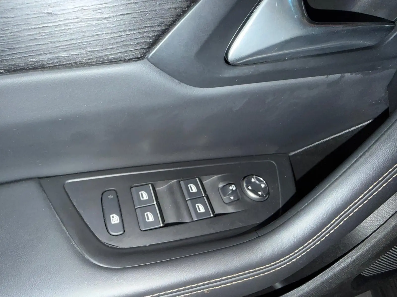 Gros plan sur les commandes de lève-vitres et rétroviseurs électriques sur la porte côté gauche en cuir noir.