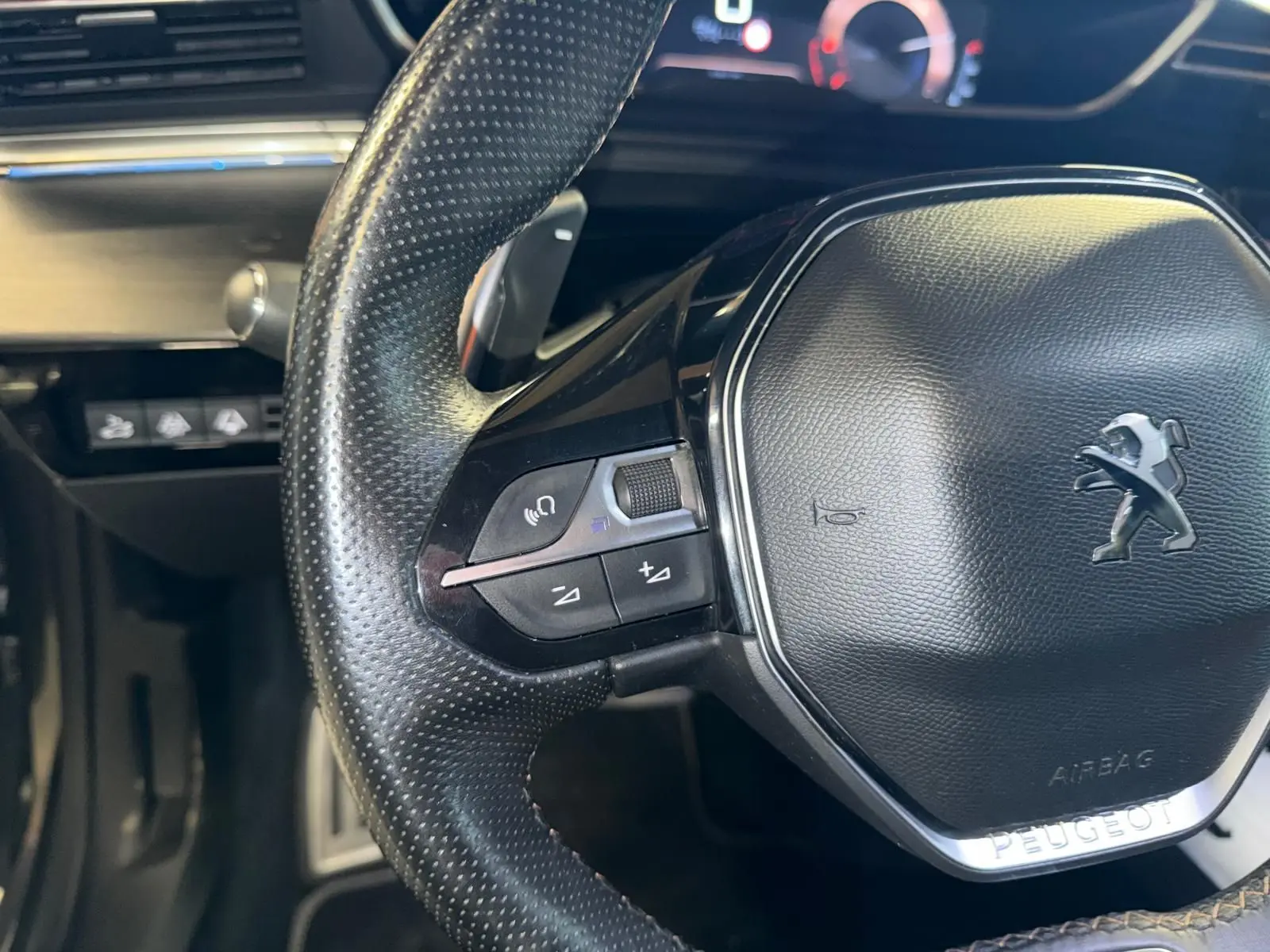 Gros plan sur le volant cuir perforé de la Peugeot 508 gris, avec commandes intégrées et logo lion au centre.