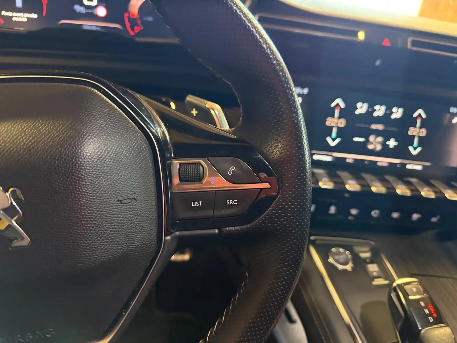 Gros plan sur le volant cuir noir et les commandes multifonctions, avec écran tactile et console bois gris en arrière-plan.