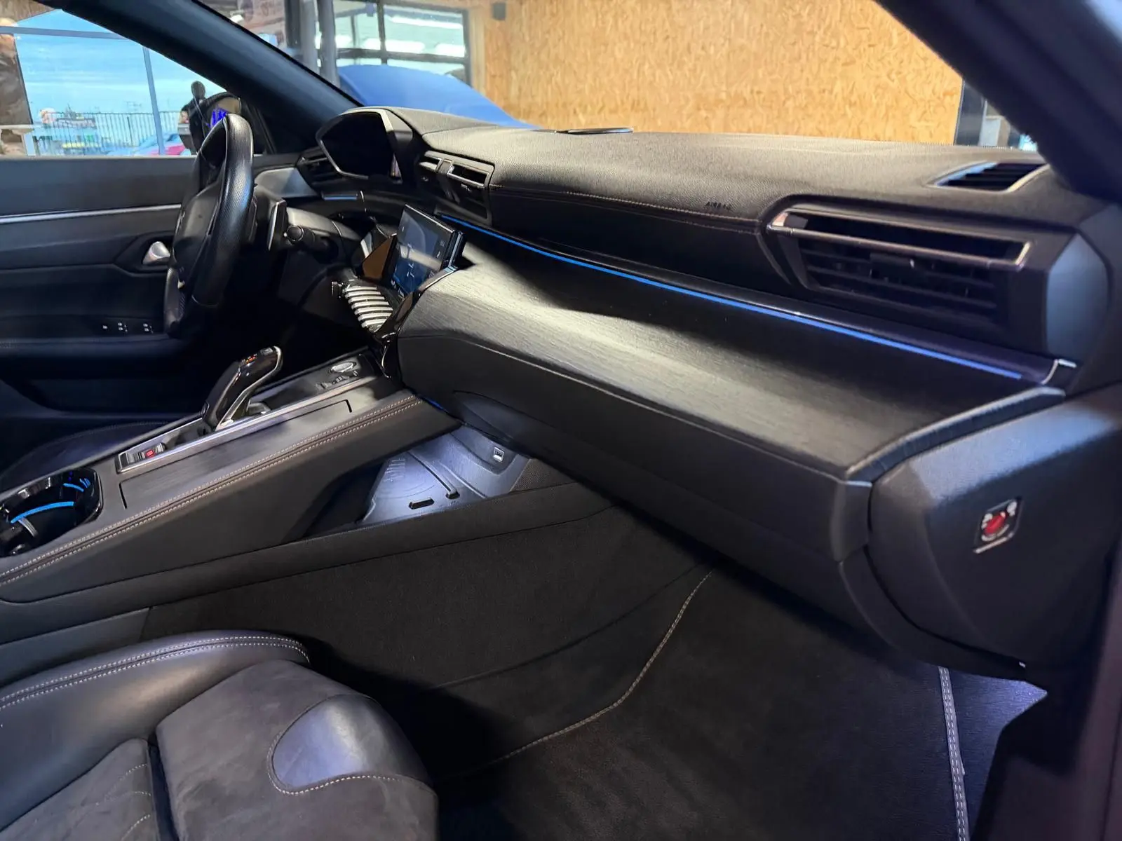 Intérieur avant droit de la Peugeot 508 gris, avec tableau de bord en bois, éclairage d'ambiance bleu et sellerie cuir noir.