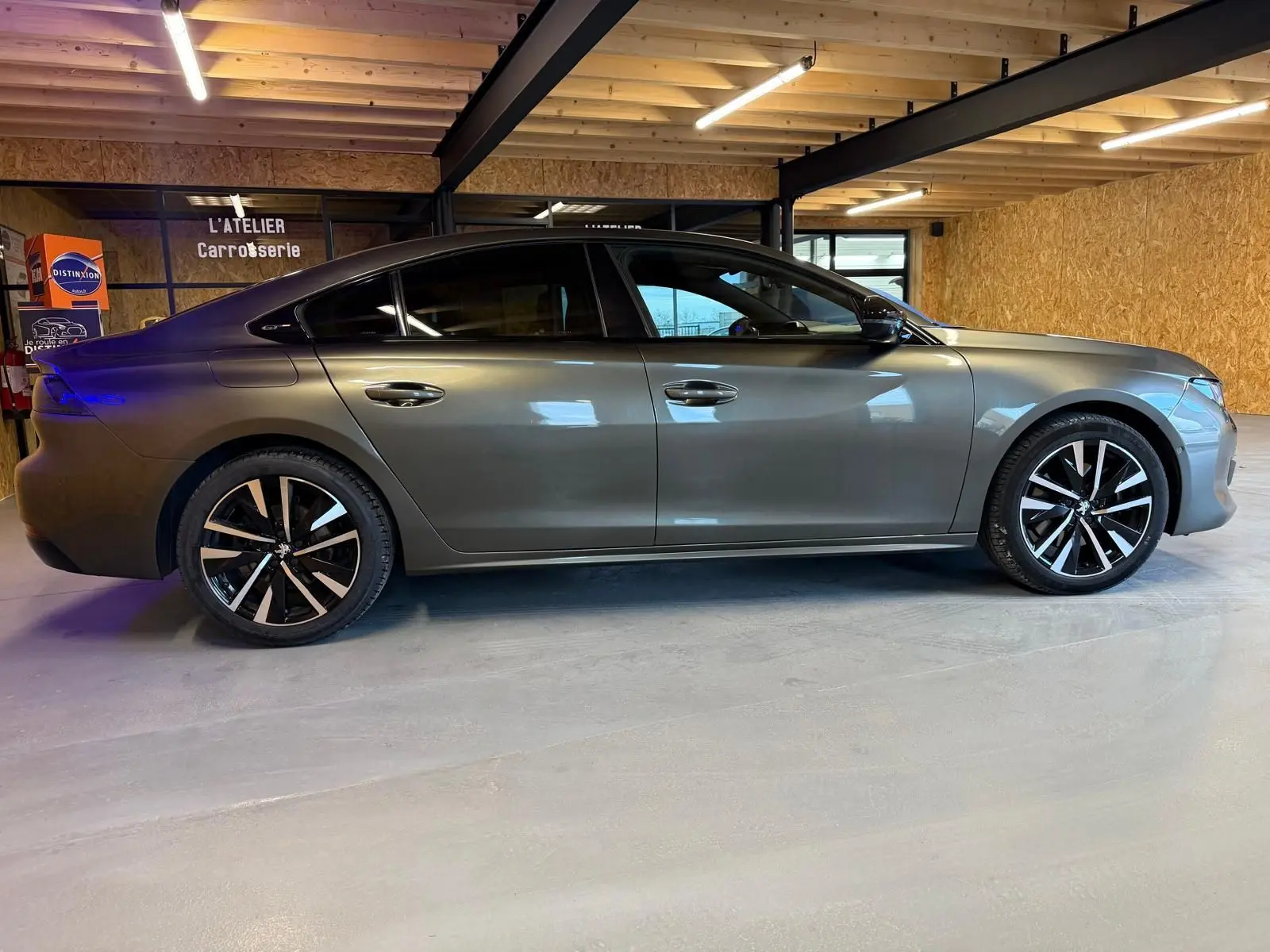 Profil droit d'une Peugeot 508 gris métallisé avec jantes alu noires et toit noir dans un garage.