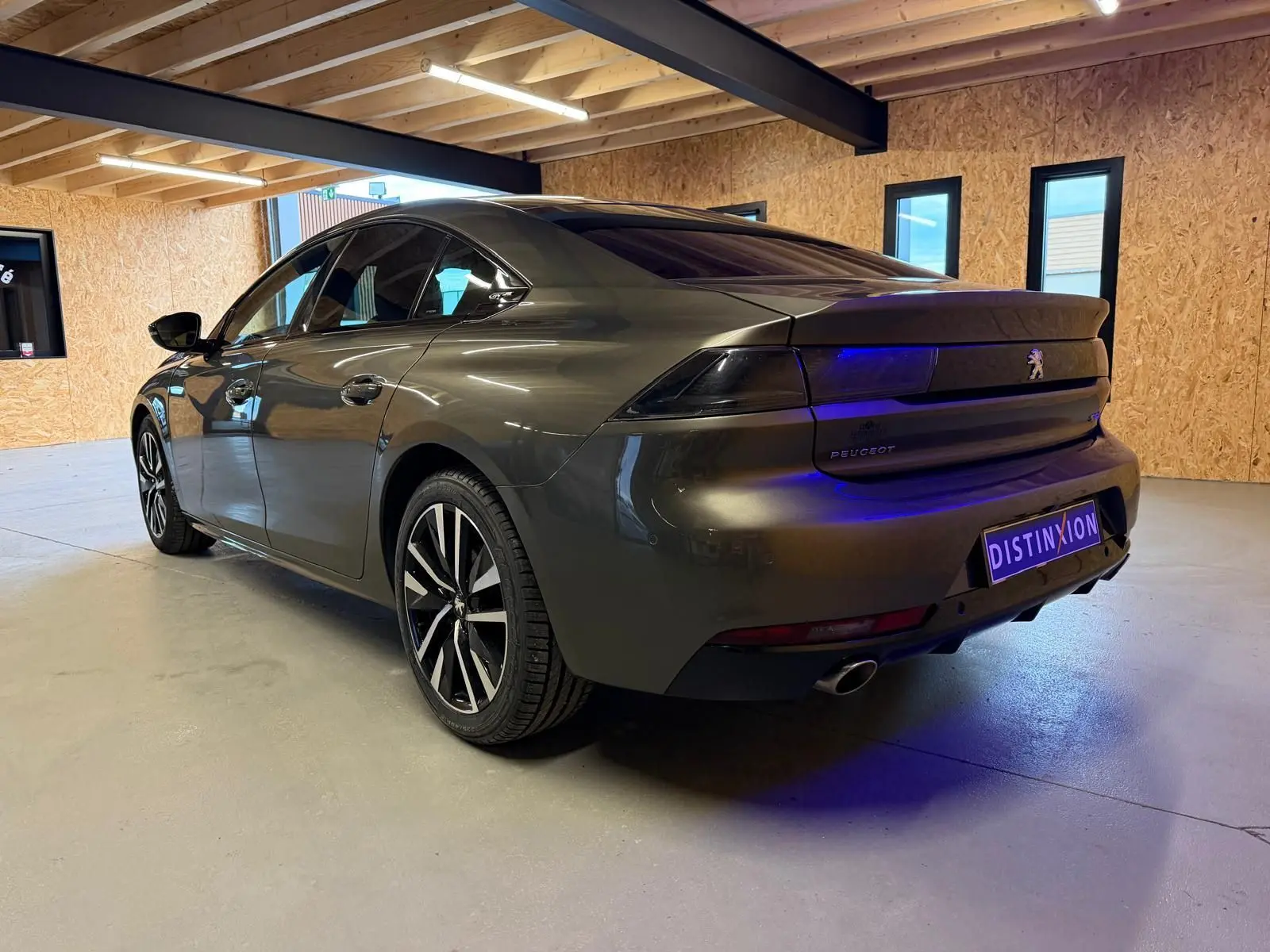 Vue 3/4 arrière droite d'une Peugeot 508 gris métallisé avec jantes alu et feux arrière à LED dans un garage.