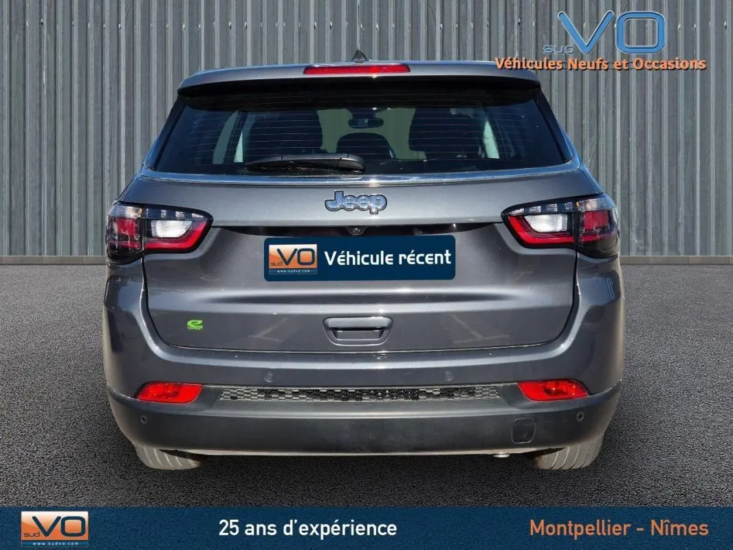 Vue arrière d'un Jeep Compass gris 2024 avec feux LED et logo e-Hybrid visible sur un fond neutre.