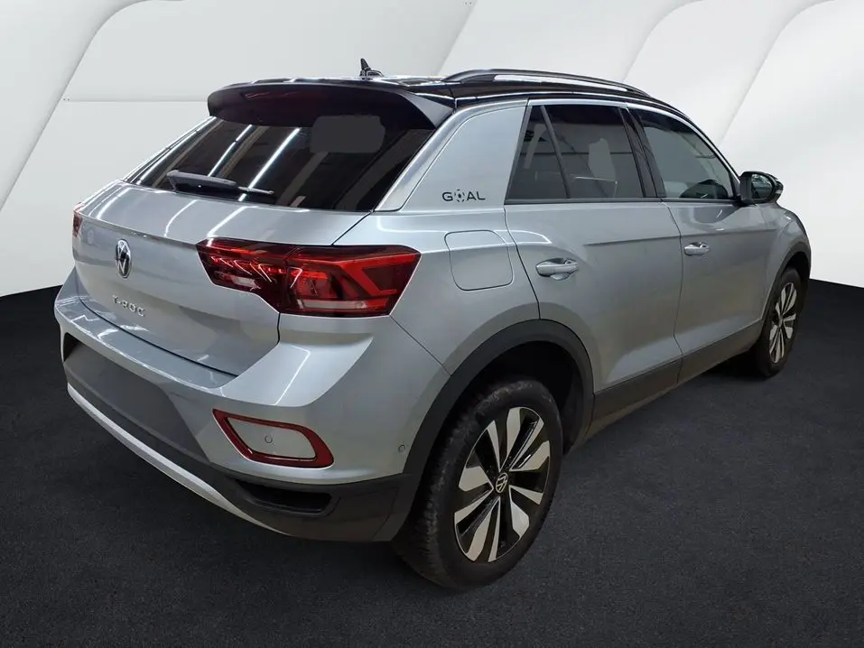 Volkswagen T-Roc gris clair en 3/4 arrière droit, avec toit noir et jantes alliage distinctives.