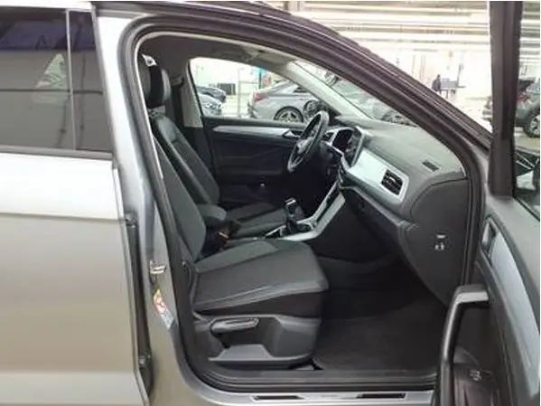 Vue intérieure côté conducteur du Volkswagen T-Roc gris clair 2025, avec sièges tissu noir et tableau de bord moderne.