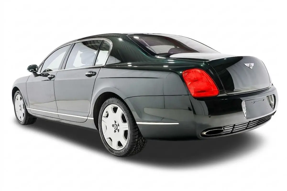 Vue 3/4 arrière droite d'une Bentley Continental Flying Spur vert foncé avec feux arrière rouges et jantes blanches.