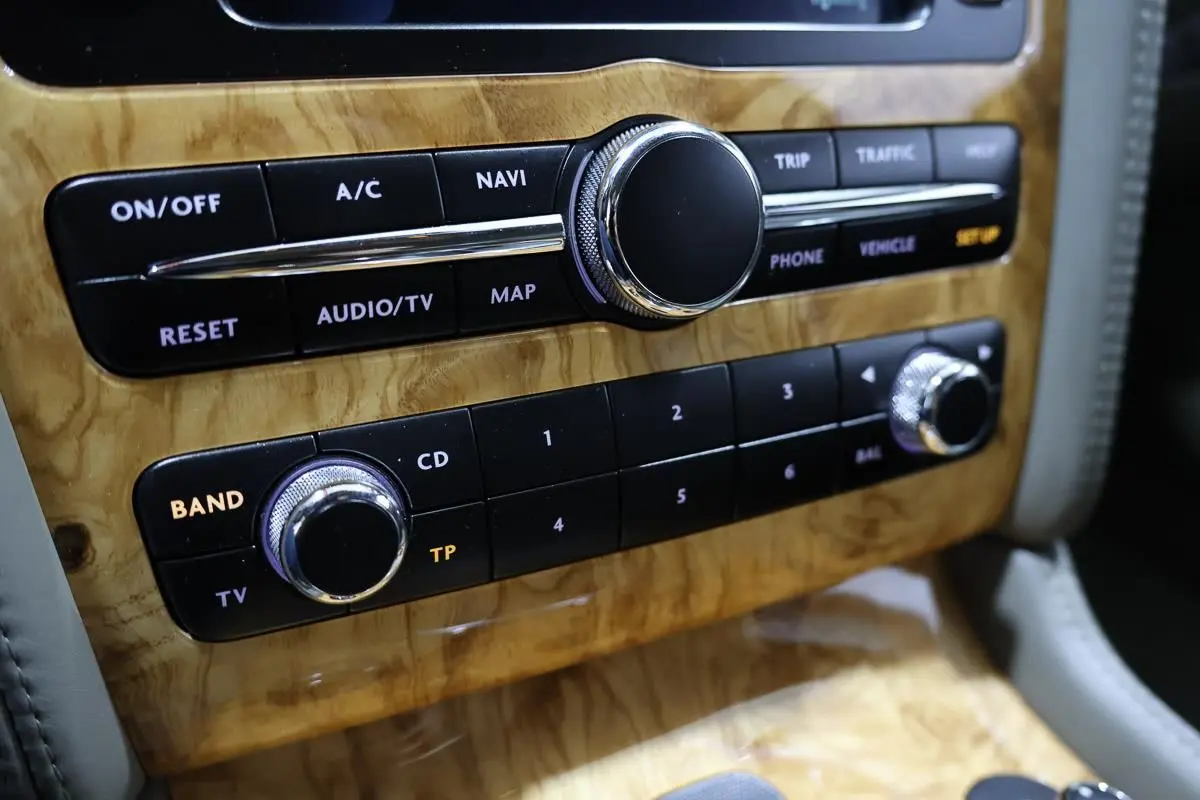 Gros plan sur la console centrale en bois clair avec commandes audio et navigation de la Bentley Continental Flying Spur.