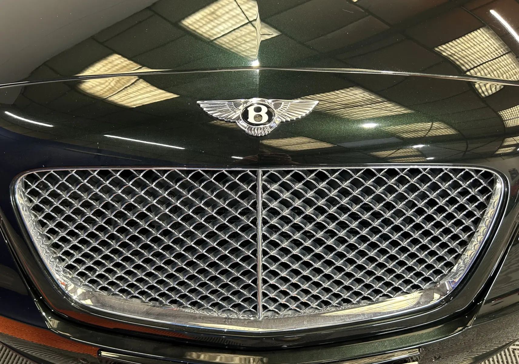 Gros plan sur la calandre chromée et l'emblème Bentley d'une Continental Flying Spur vert foncé, vue de face.