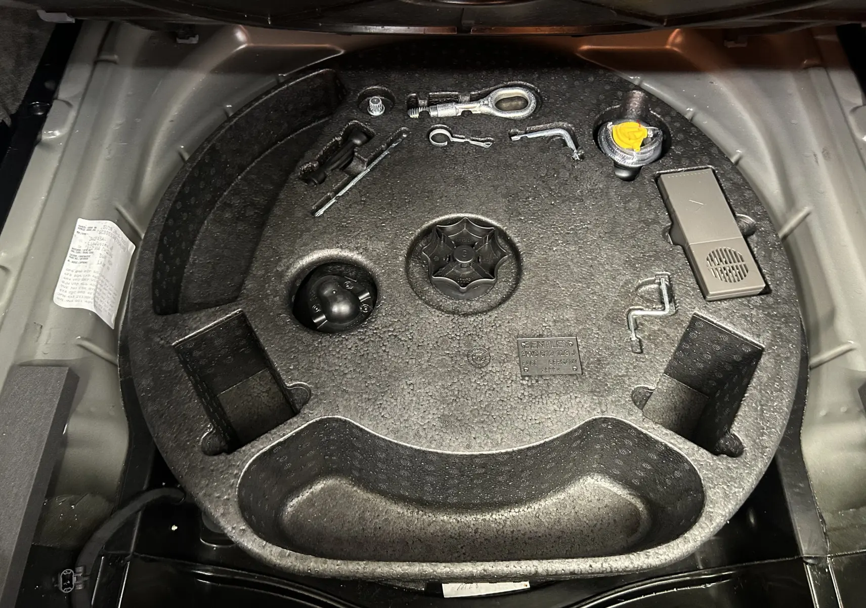 Coffre ouvert montrant le rangement d'outils et accessoires d'origine Bentley sur fond gris clair.