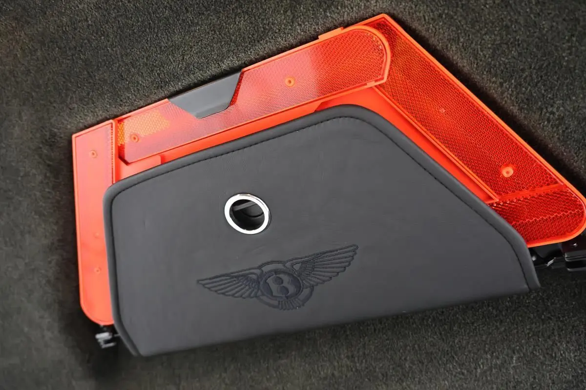 Détail du coffre avec triangle de sécurité rouge et housse noire siglée Bentley sur un Continental Flying Spur vert foncé.