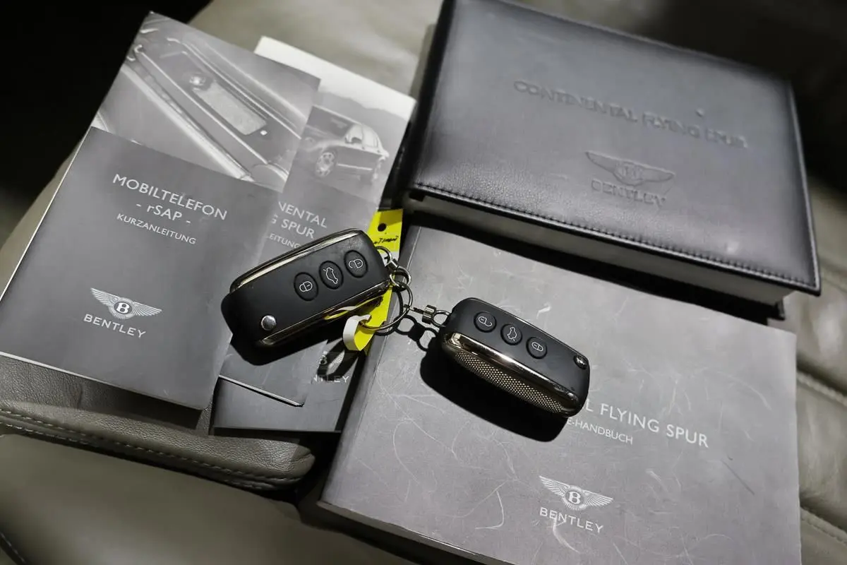 Vue rapprochée sur les clés et les manuels noirs du Bentley Continental Flying Spur posés sur un siège en cuir gris.
