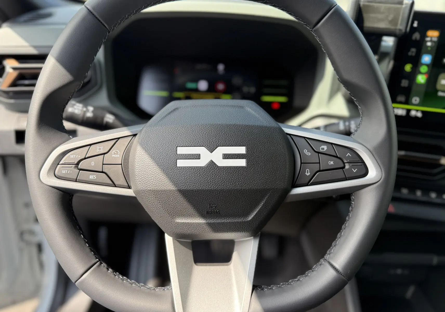 Gros plan sur le volant noir du Dacia Duster Hybrid 155 Extreme 2026, avec commandes intégrées et tableau de bord flou en arrière-plan.