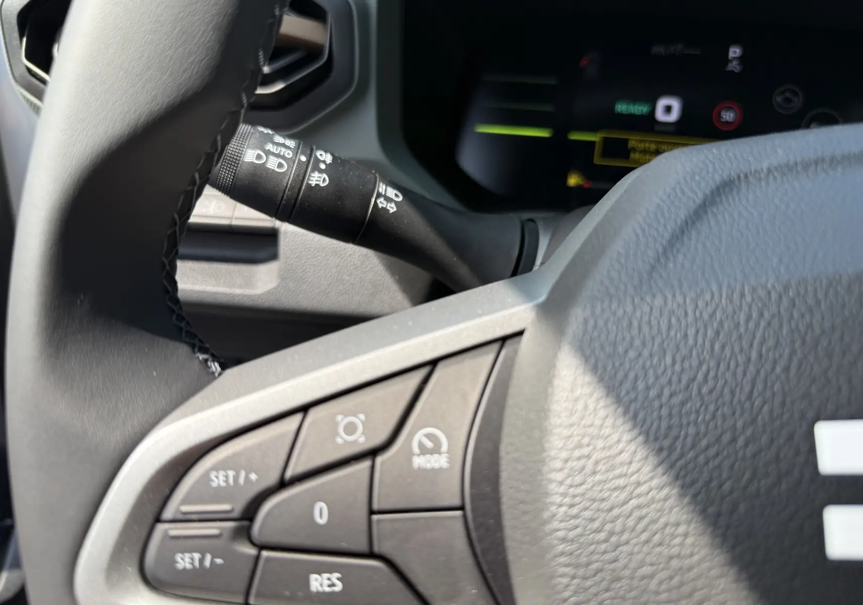 Gros plan sur le volant et la commande de régulateur de vitesse du Dacia Duster Hybrid 155, intérieur noir texturé.