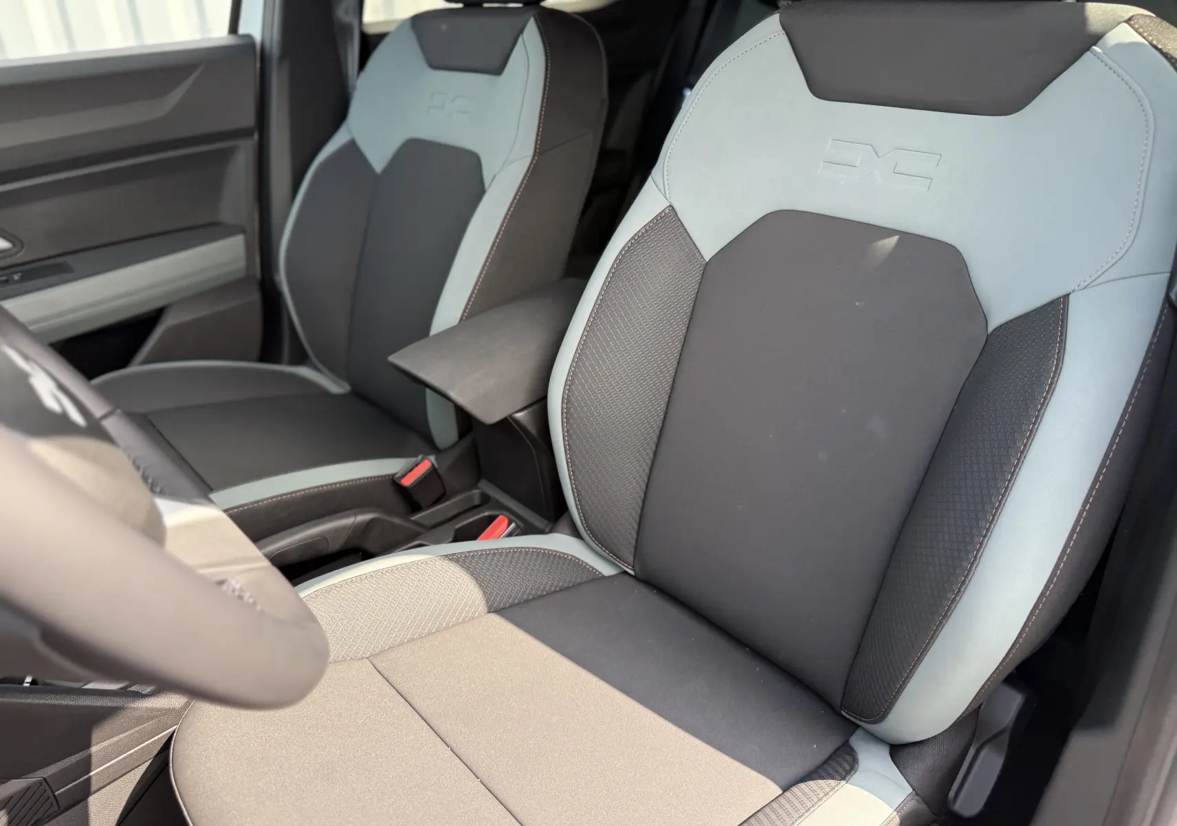 Vue rapprochée des sièges avant tissu noir et gris clair du Dacia Duster Hybrid 155 Extreme 2026, avec accoudoir central.
