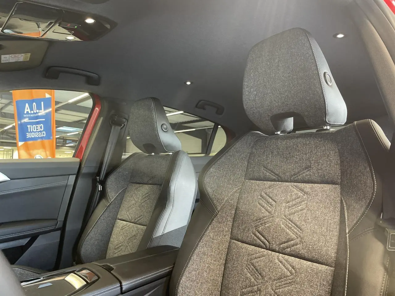 Vue intérieure côté avant droit de la Renault Rafale 2025, sièges sport gris avec motifs embossés et accoudoir central noir.