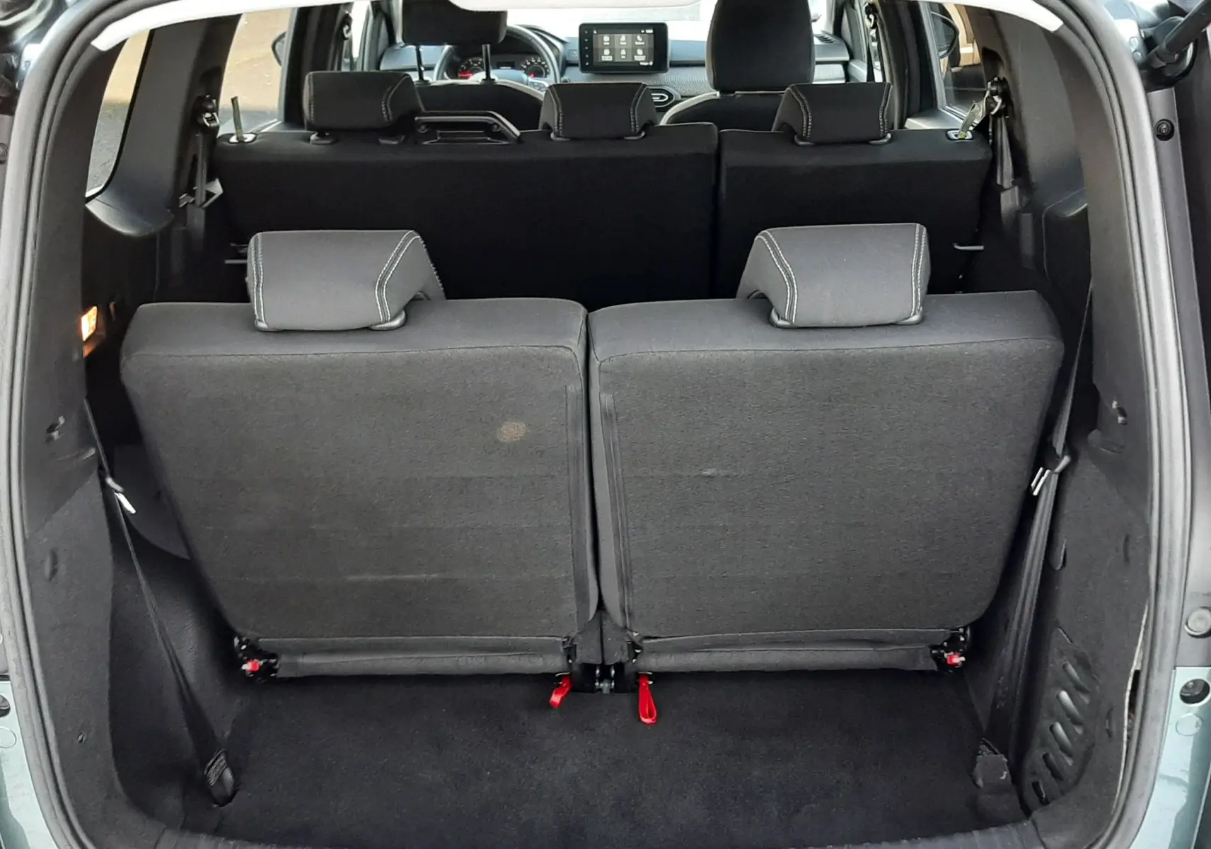 Vue arrière du coffre ouvert d'un Dacia Jogger vert cèdre métal 2025, montrant les sièges arrière rabattus et l'intérieur noir.