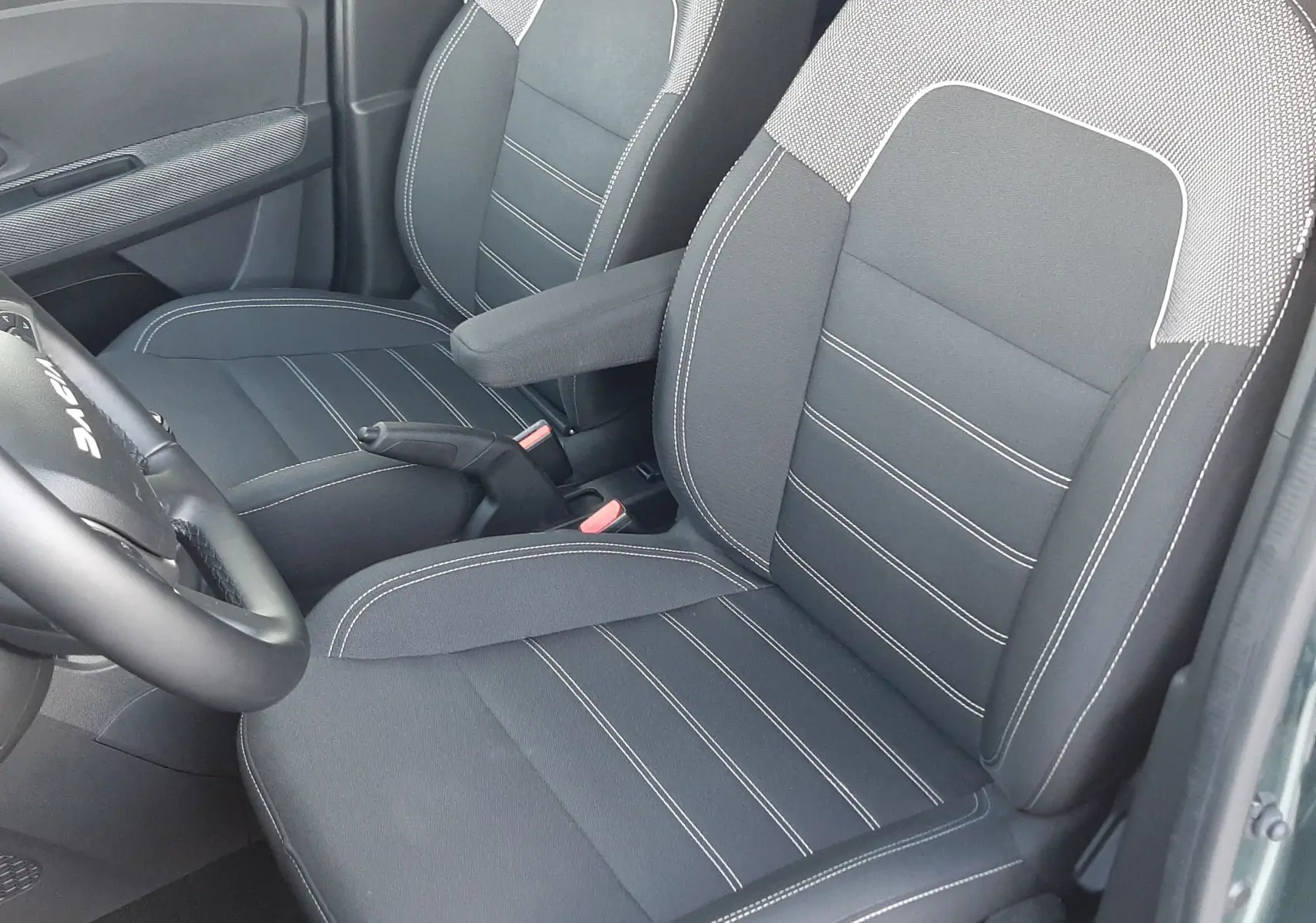 Vue intérieure côté conducteur montrant les sièges avant en tissu noir avec surpiqûres blanches du Dacia Jogger vert cèdre 2025.