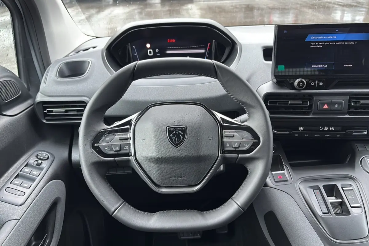 Vue intérieure centrée sur le volant cuir multifonctions du Peugeot Rifter gris Artense avec tableau de bord digital.