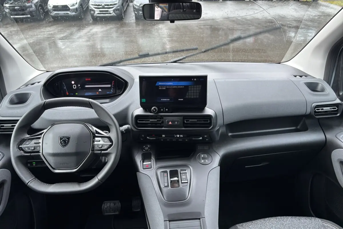 Vue intérieure avant du Peugeot Rifter gris Artense 2026, tableau de bord moderne avec écran tactile central et volant multifonctions cuir.