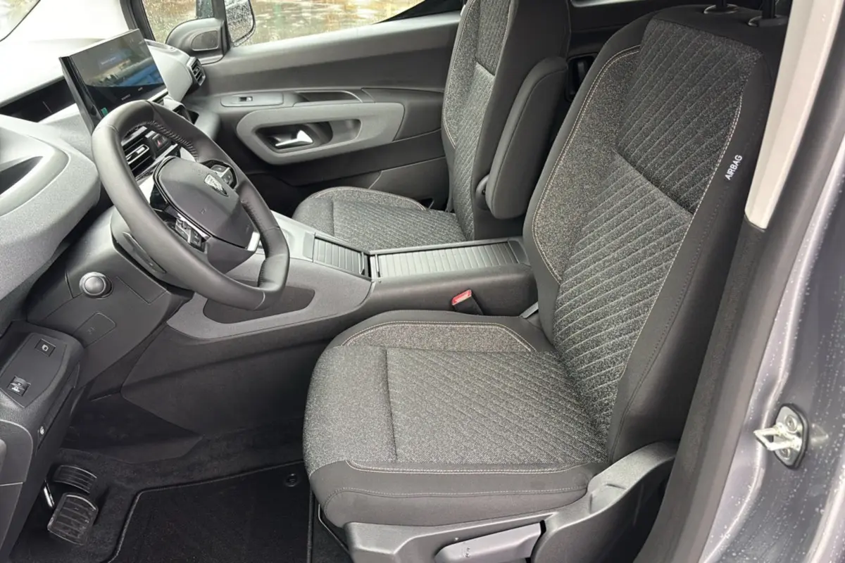 Vue intérieure côté conducteur du Peugeot Rifter 2026, sièges tissu gris et volant cuir multifonctions.