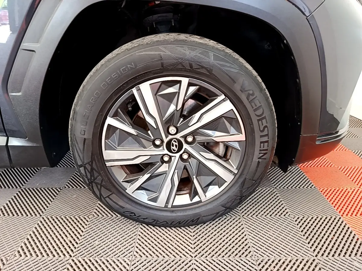 Gros plan sur la roue avant droite d’un Hyundai Tucson gris foncé avec jante alliage au design géométrique.