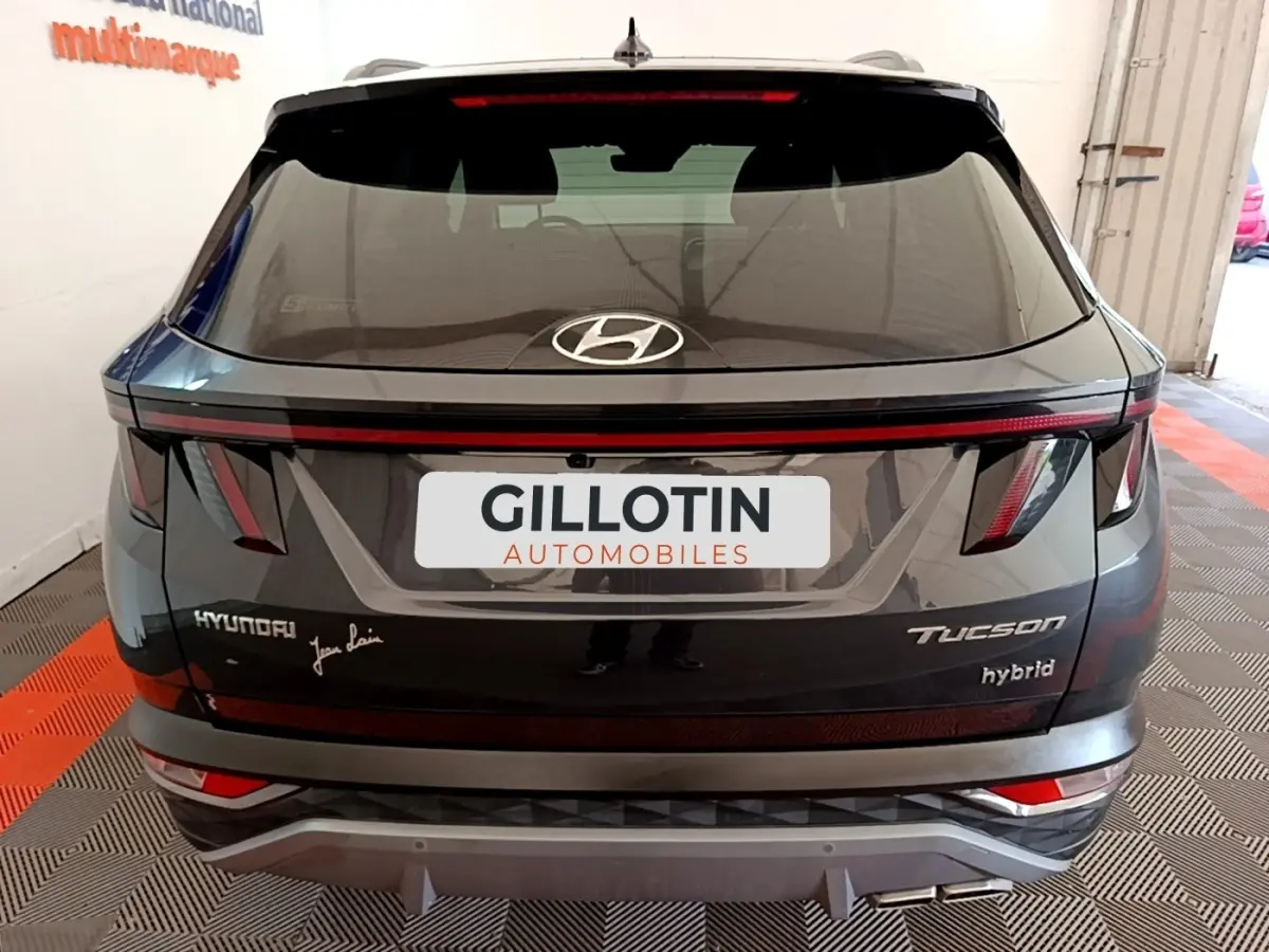 Vue arrière d’un Hyundai Tucson gris foncé hybride 2022 avec feux arrière en bandeau et logo Hyundai visible.