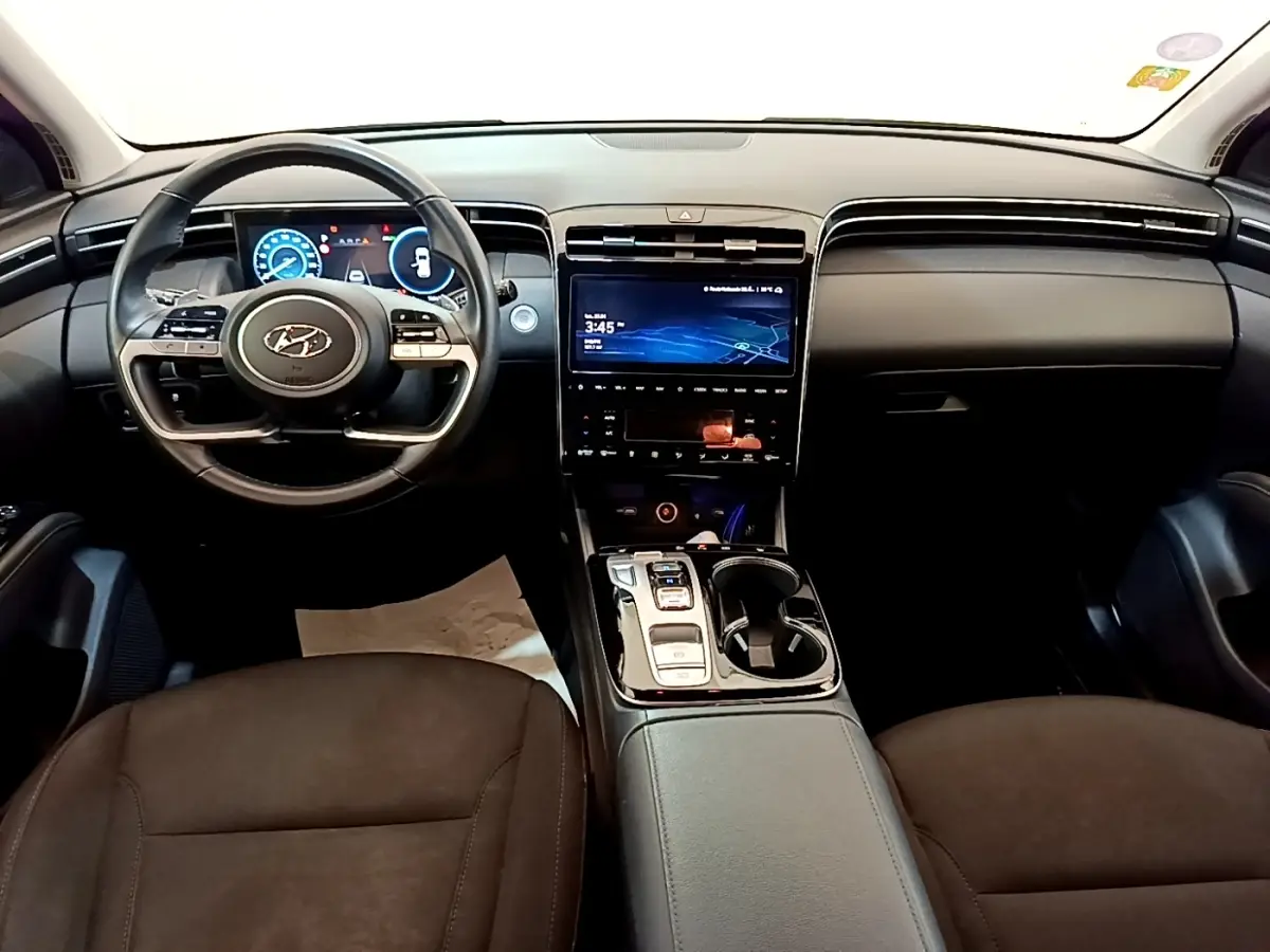 Vue intérieure avant du Hyundai Tucson 1.6 Hybrid 230 Creative 2022, tableau de bord noir avec écran tactile central et volant multifonctions.
