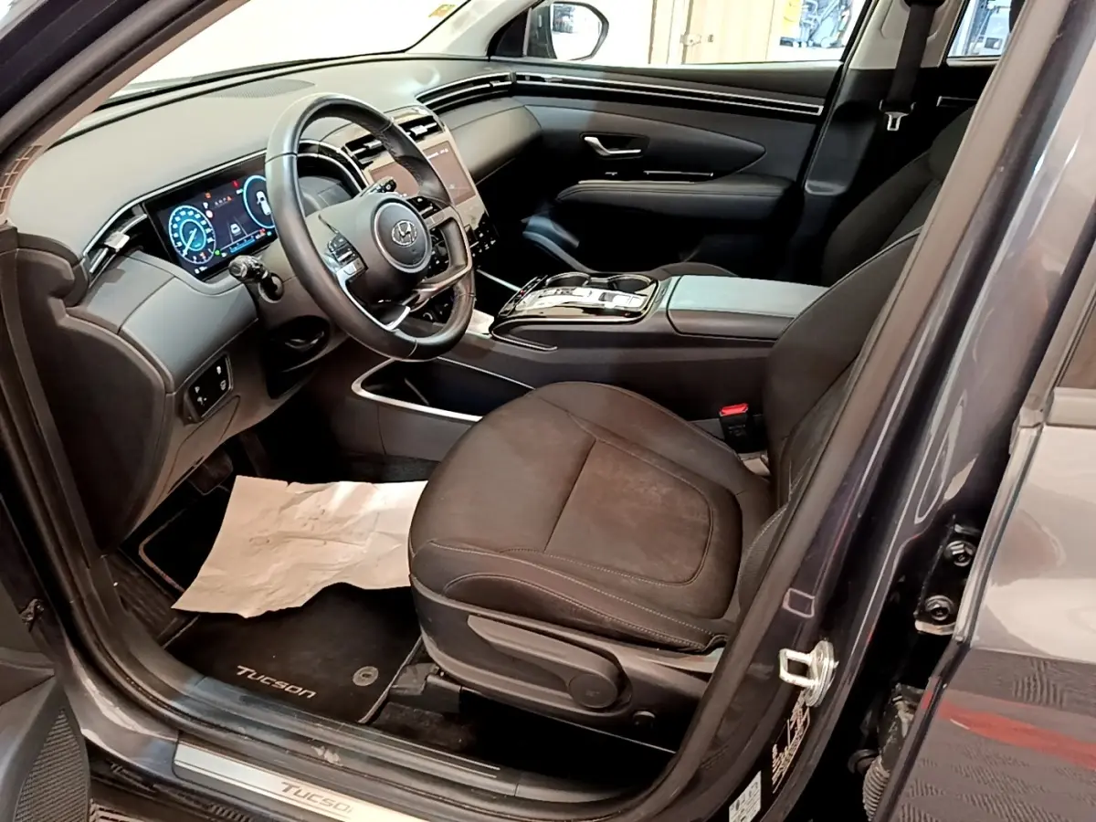 Vue intérieure côté conducteur du Hyundai Tucson gris foncé 2022, mettant en valeur le tableau de bord digital et les sièges noirs.