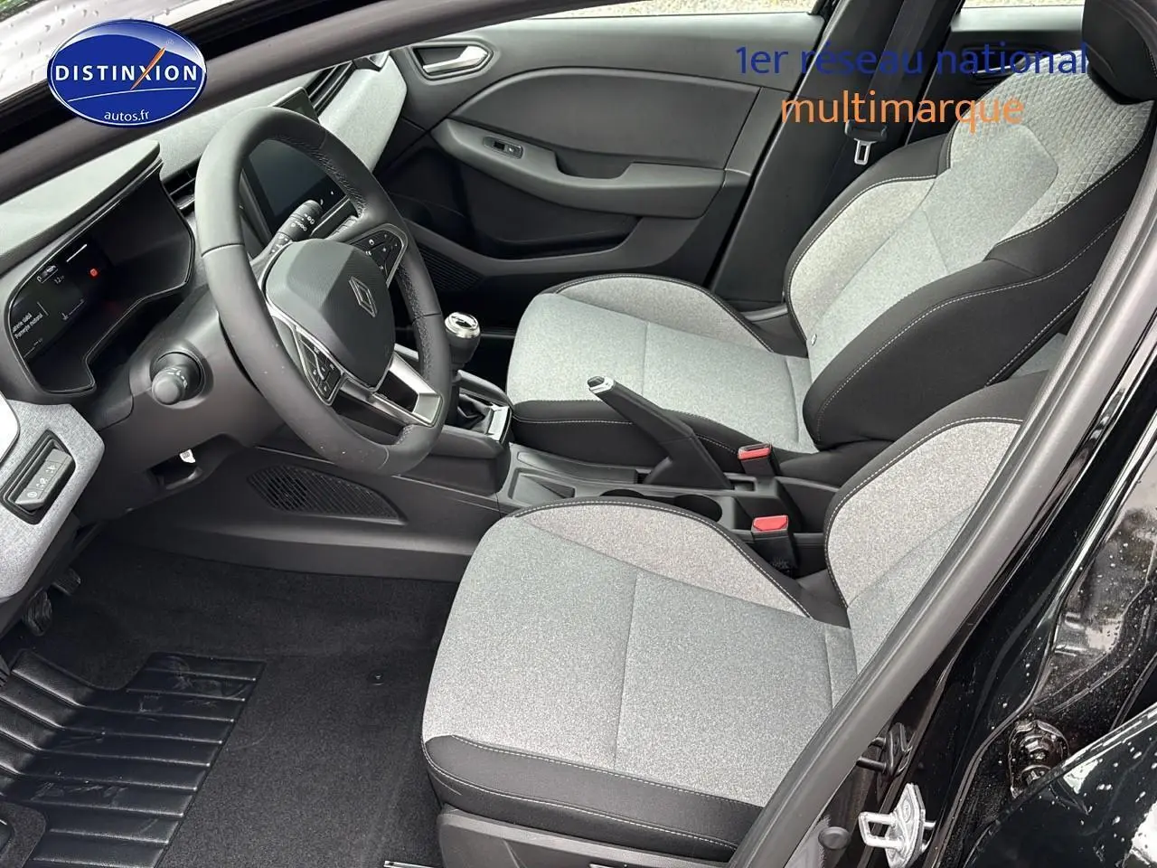 Intérieur avant droit d'une Renault Clio V 2025 noir étoilé, sièges gris clair et volant cuir avec boîte manuelle.