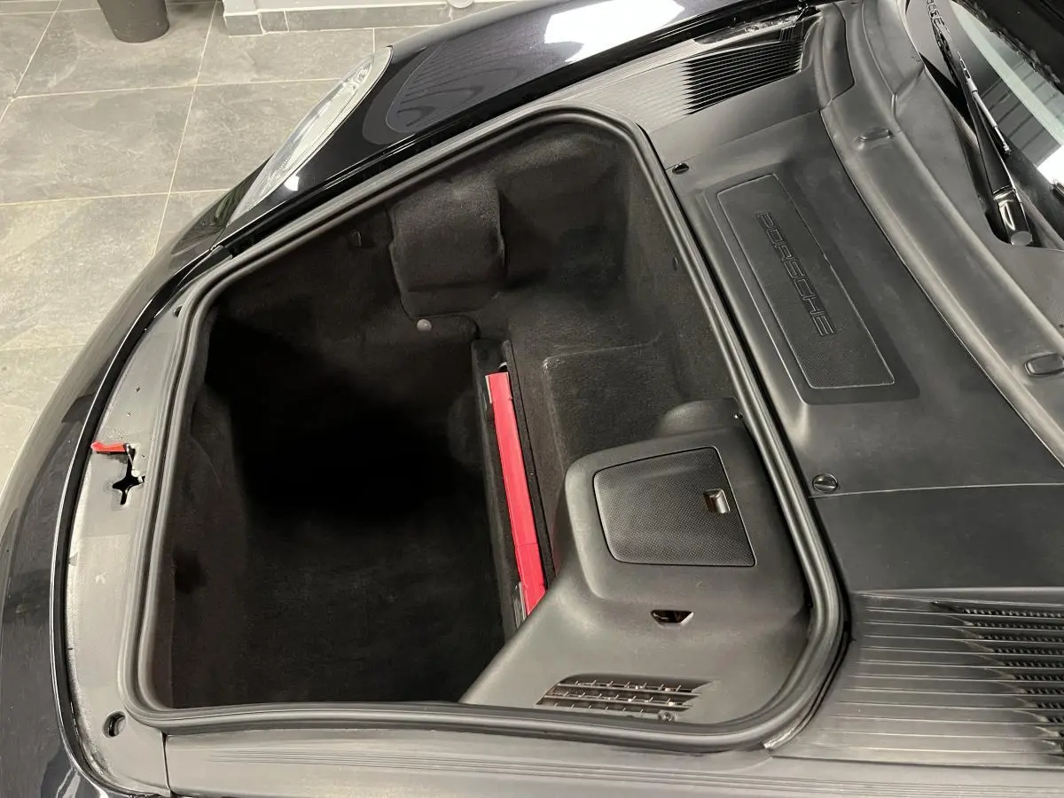 Vue plongeante sur le coffre avant noir ouvert d'une Porsche Cayman 987 2.7i avec intérieur propre et compartiments visibles.