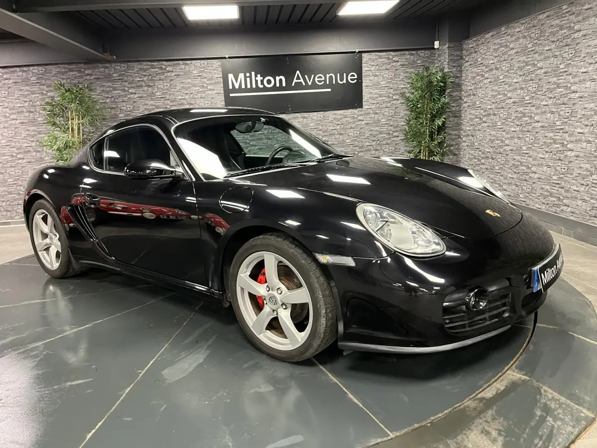 Porsche Cayman noir vue 3/4 avant droit avec jantes 18 pouces et étriers de frein rouges dans un showroom.