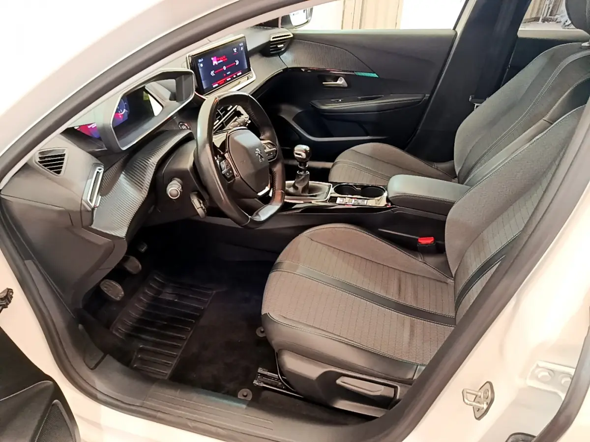 Intérieur côté conducteur d'une Peugeot 208 blanche, avec tableau de bord numérique et sièges tissu gris.