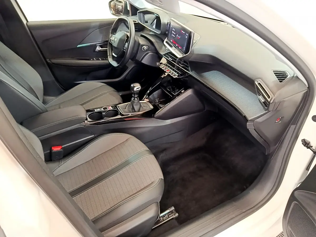 Intérieur de la Peugeot 208 blanche, vue côté conducteur, tableau de bord moderne avec écran tactile et volant cuir.