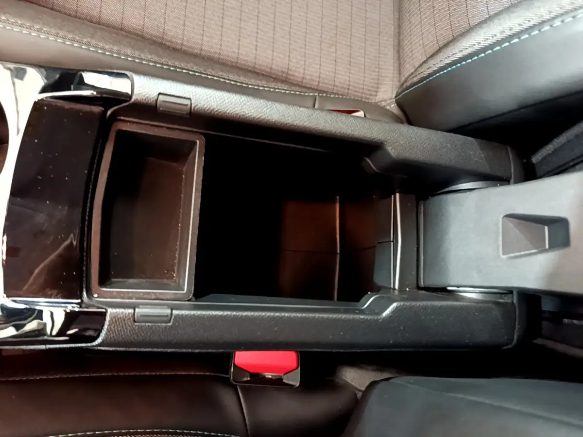 Vue plongeante sur la console centrale noire ouverte du Peugeot 208 blanc, montrant le rangement intérieur et le frein à main électrique.