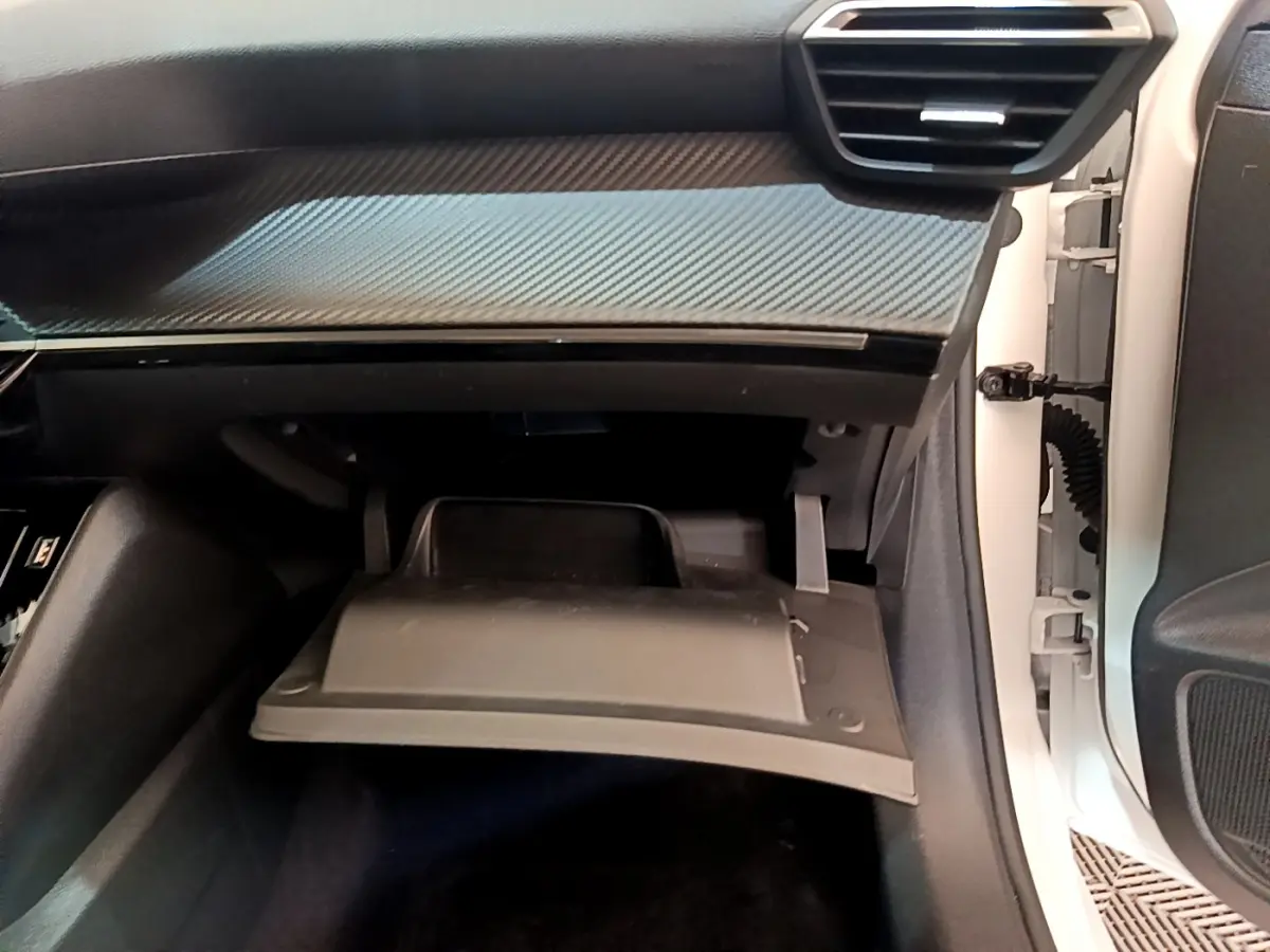 Vue intérieure côté passager du coffre à gants ouvert avec tableau de bord noir et insert effet carbone sur Peugeot 208 blanc
