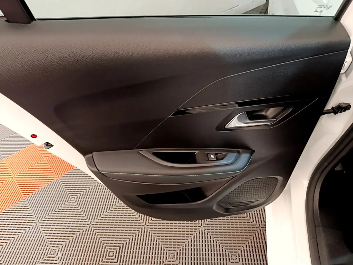 Porte intérieure côté gauche noire de la Peugeot 208 blanche, avec poignée argentée et commande de vitre électrique.