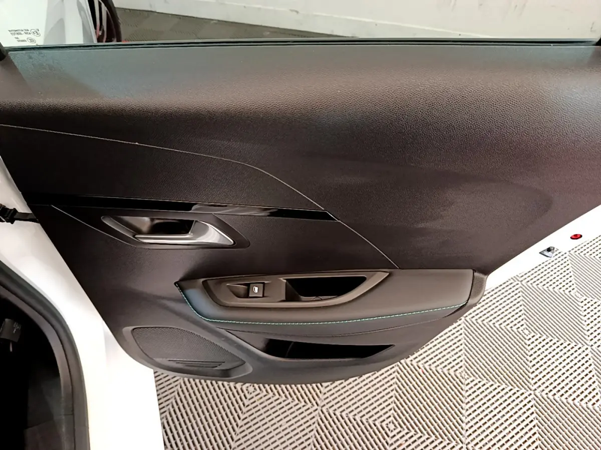 Vue rapprochée de la porte avant gauche noire de la Peugeot 208 blanche, avec poignée et commande de vitre intégrées.